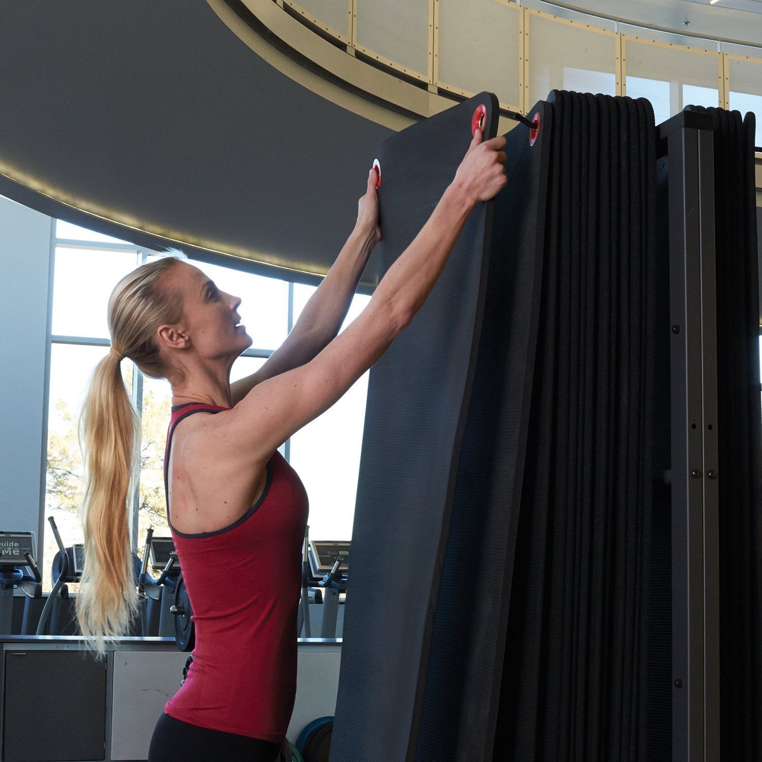 Woman hanging the Hanging Mats (3/8") on a wall mounted rack